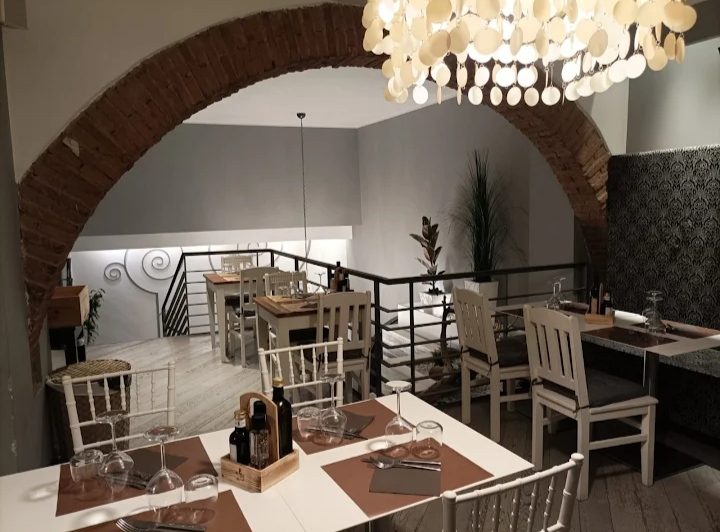 L'arco in mattoni che divide le due sale, con il soppalco e la scala sul fondo e un lampadario a dischi chiari.